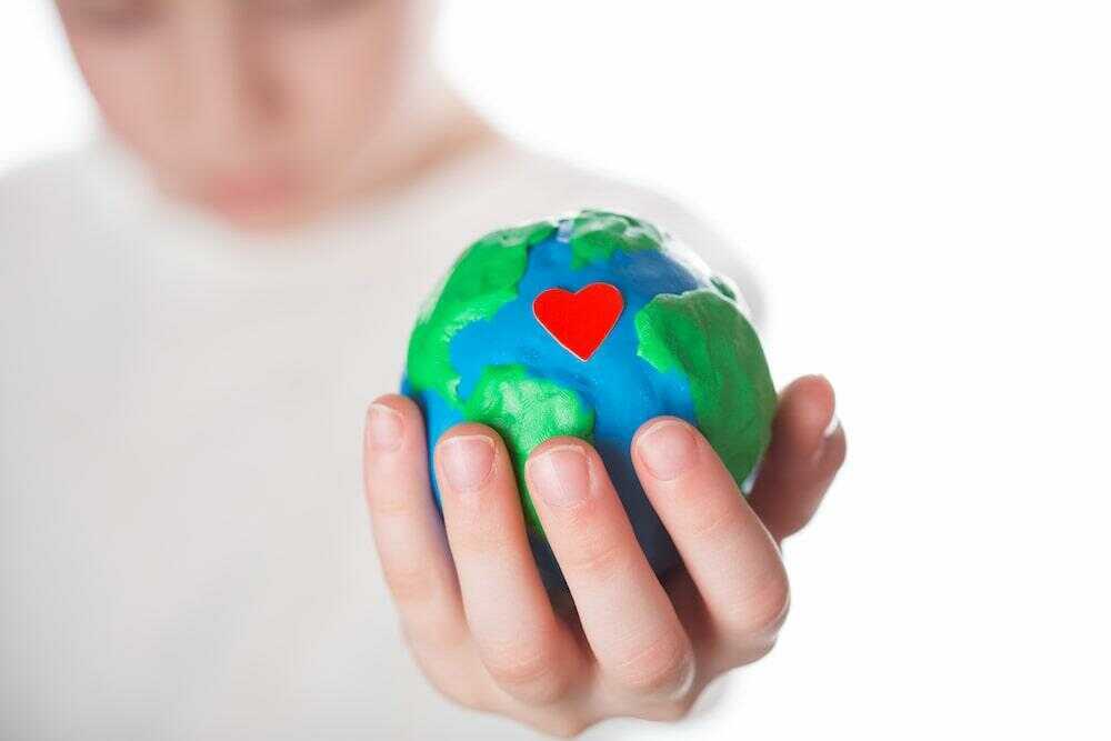 Une main tenant une sculpture de la terre avec un coeur dessus